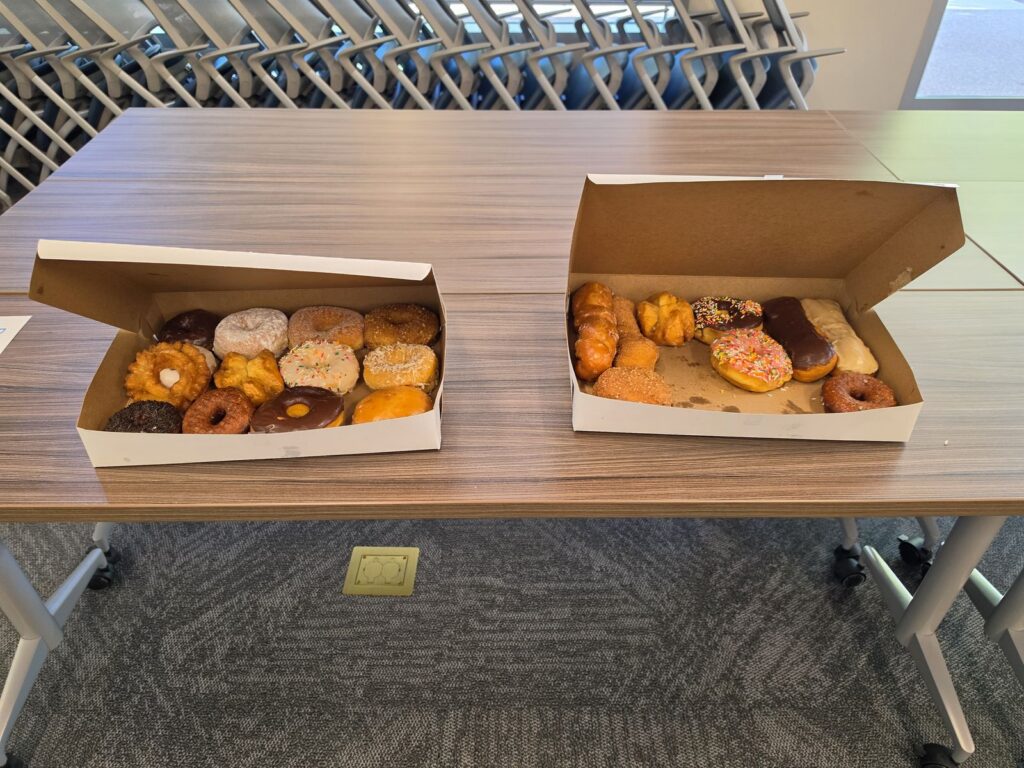 Two open boxes of assorted donuts on a table, set out for attendees.