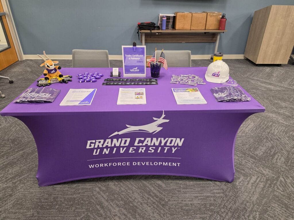 Grand Canyon University Workforce Development table with trades certificate flyers, branded giveaways, small American flags and a hard hat.