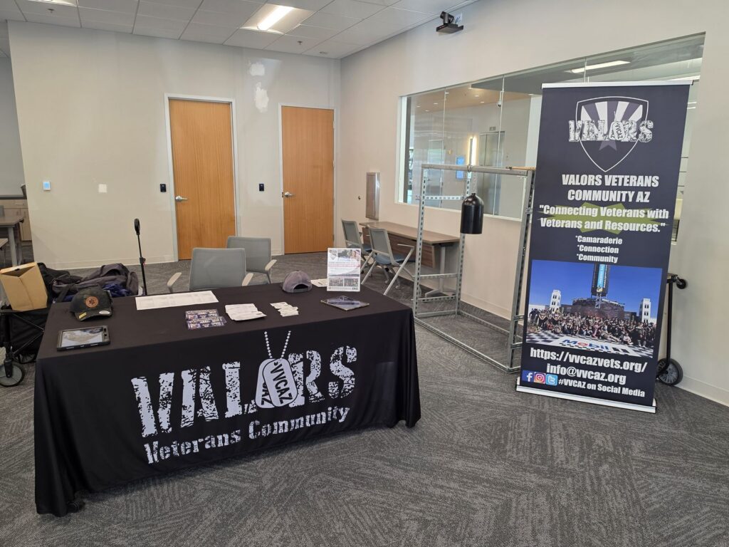 The VVCAZ table with a black Valors Veterans Community tablecloth, flyers and a tablet, set up beside the VVCAZ pull-up banner.