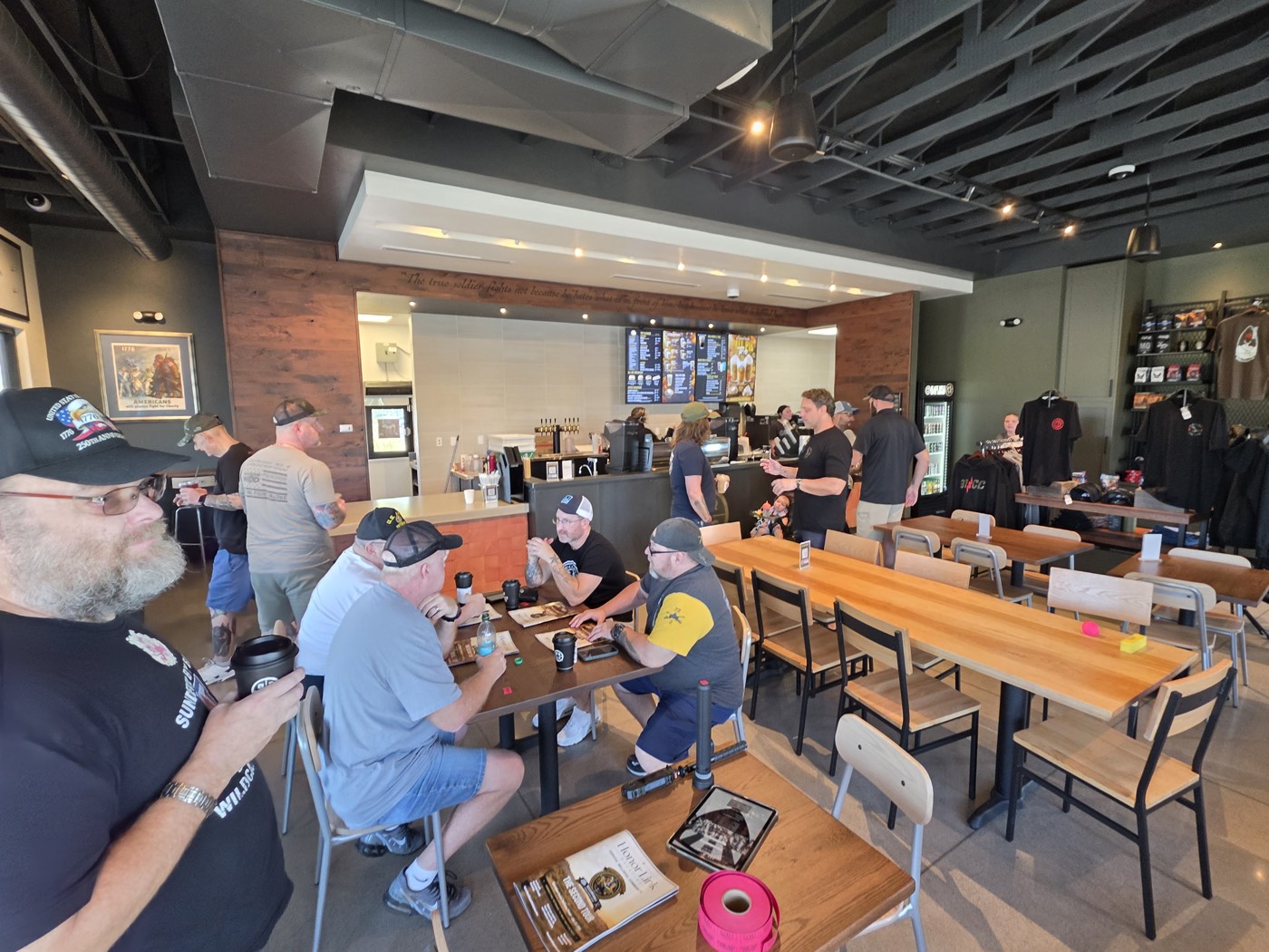 Wide view of Black Rifle Coffee in Tucson with veterans seated and standing at wooden tables during Coffee Connections.