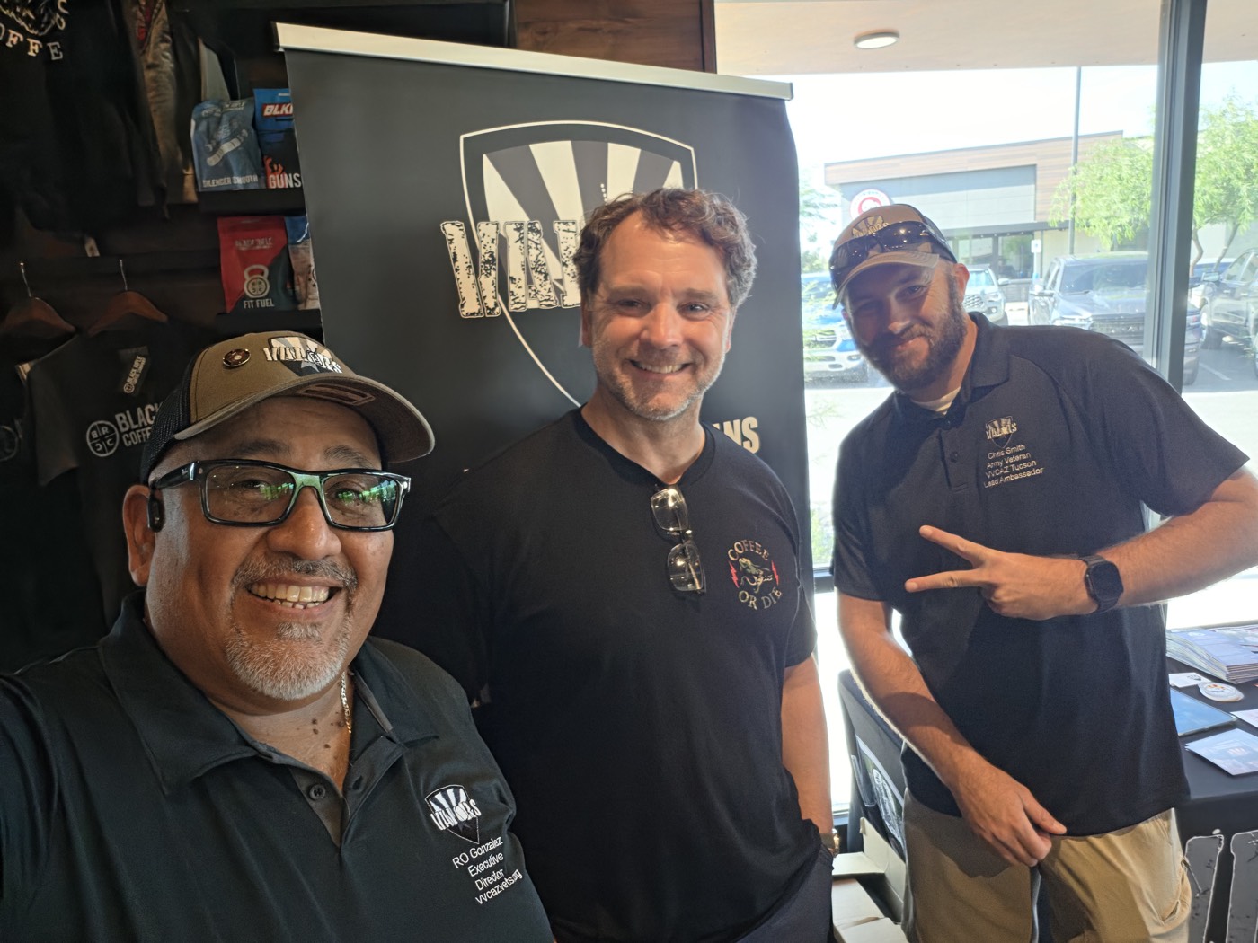 Ro Gonzalez, Executive Director of Valors Veterans Community AZ, takes a selfie with two attendees in front of the VVCAZ banner at Black Rifle Coffee in Tucson.